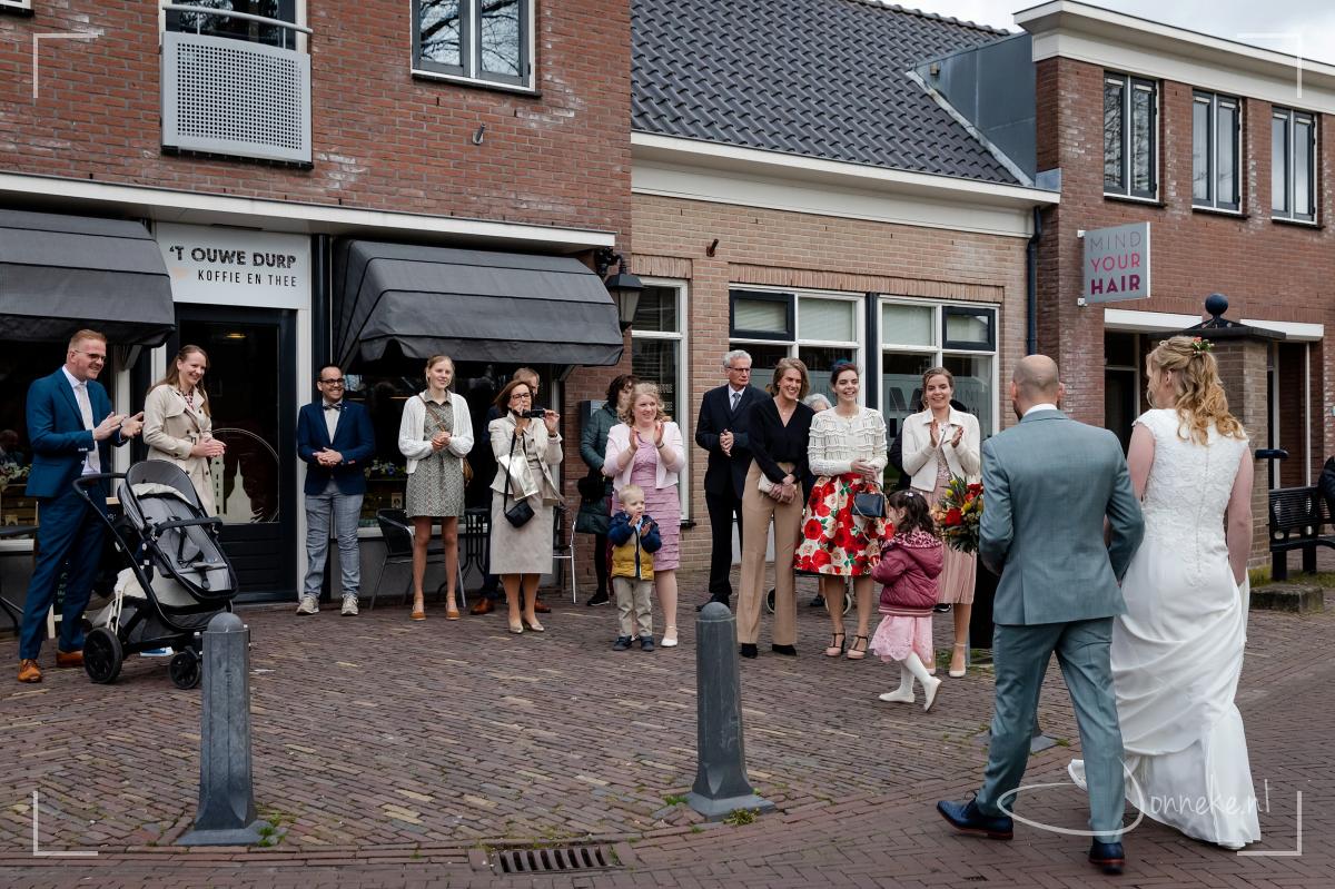Ouders, broers en zussen staan het bruidspaar op te wachten. Het waait hard, maar het is droog!