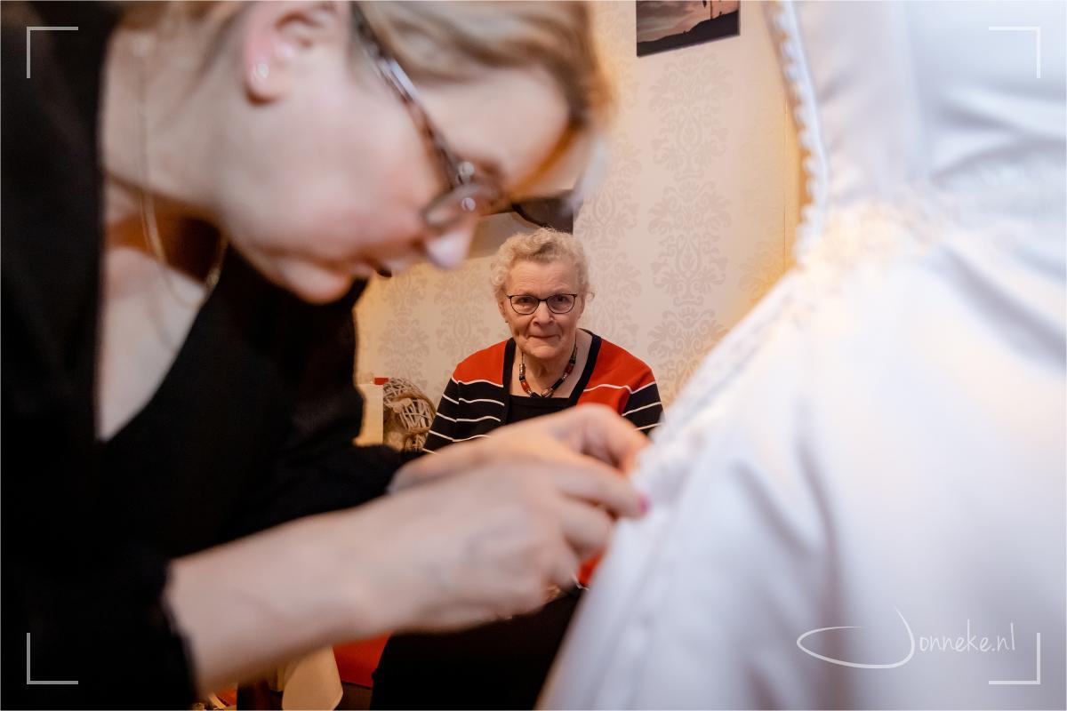 Mam kijkt oplettend toe hoe de jurk dichtgeknoopt wordt door de buurvrouw.